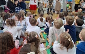 Dzieci siedzące na podłodze, kobiety oraz Miś Uszatek.