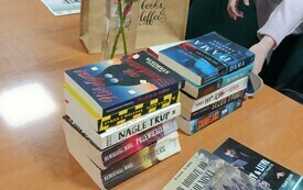 Na stoliku ksiażki, kwiaty i kobieta.