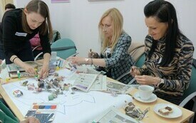 Trzy kobiety wyklejają z kawałków gazet kota.