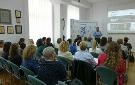Mężczyzna z zarostem, w niebieskiej koszuli przemawia do zebranej publiczności