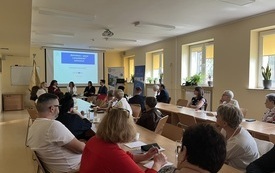 Uczestnicy seminarium siedzą przy stołach zwróceni w kierunku ekranu projekcyjnego na którym wyświetlana jest prezentacja