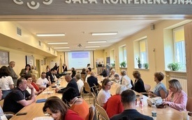 Grupa ludzi siedząca przy stolikach w sali konferencyjnej